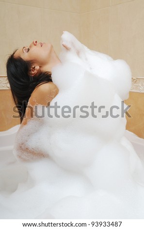 Woman is covered with a foam bath. She is taking a bath. She is washing and relaxing.