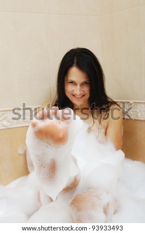 Woman is covered with a foam bath. She is taking a bath. She is washing and playing and smiling.