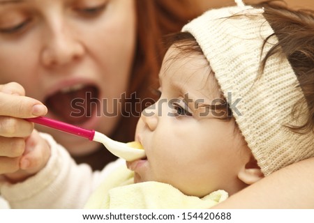 The little girl eating marrow puree from a spoon, sitting in a chair for feeding