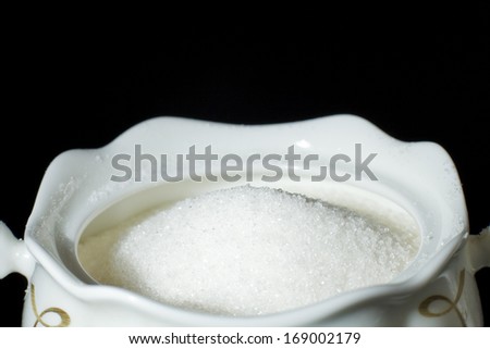 White sugar in a sugar bowl on a black background