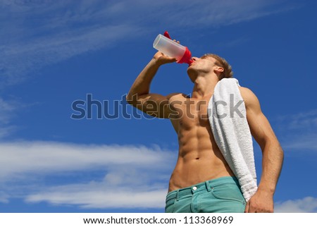 Fit young man with white towel over his shoulder, drinking water.