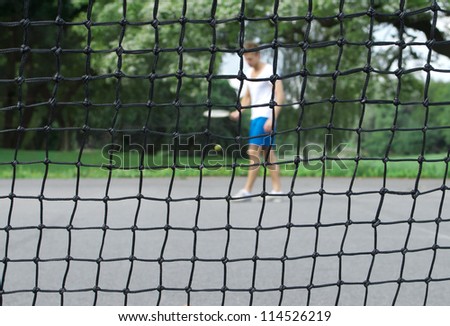 Tennis player with racket and ball seen through the tennis net. Focus on the net.