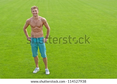Fit young man standing on green playing field, smiling.