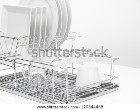 Closeup of white dishes and glasses drying on a metal dish rack.