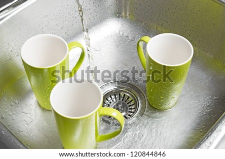 Washing bright green cups in the kitchen sink. Water running from the tap.