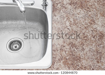 Water running from kitchen faucet. Clean new sink and countertop detail.