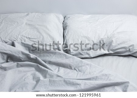 Messy bed with two pillows, gray bed linen.