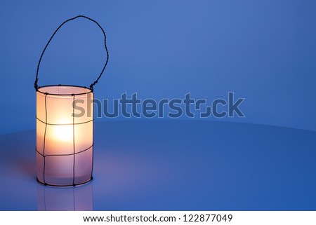 Cozy lantern on blue winter background, with copy space.