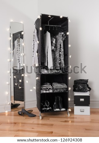 Lights decorating a mirror and a clothes organizer with black and white clothing.