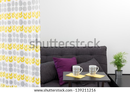 Sofa with bright cushions, behind a decorative curtain in a living room.