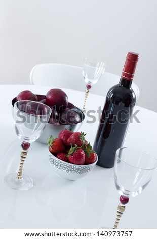 Red wine, plums and strawberries on a white table.
