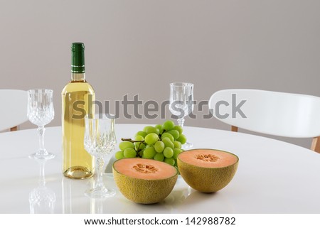 Round table with white wine, melon and green grapes.