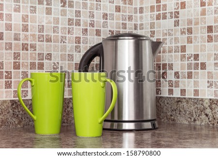 Metal electric kettle and green cups in the kitchen.