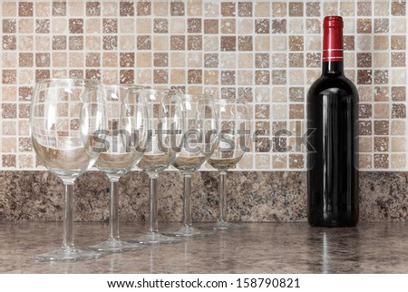 Bottle of red wine and empty glasses on kitchen countertop.