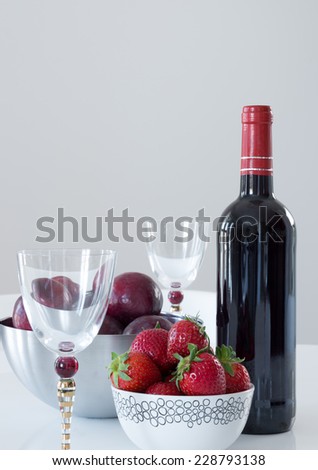 Red wine, elegant glasses, plums and strawberries on a table.