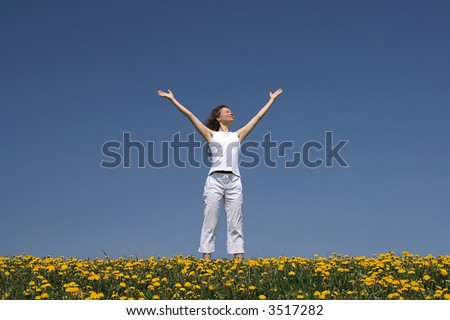 Young woman greets the sun in the morning, in a flowering spring field.