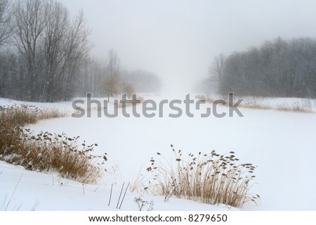 Frozen lake in gloomy misty haze of winter blizzard.
