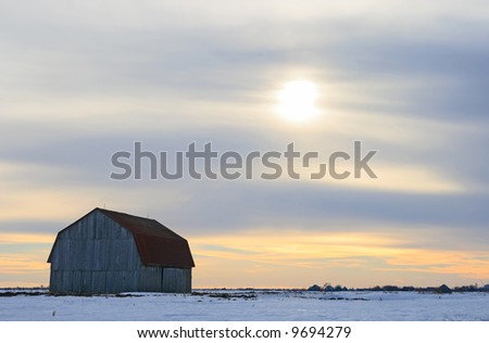 Old wooden barn in a snowy field in the evening.