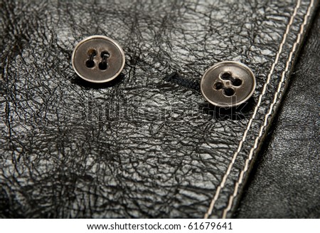 Close-up of metal buttons on shiny black leather clothing.