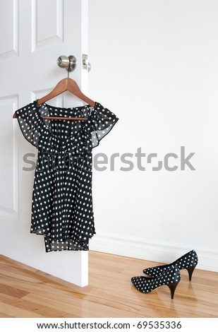 Black and white polka dot blouse on a hanger and shoes on wooden floor.