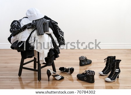 Heap of black and white clothes on a stool and disordered shoes on a wooden floor.