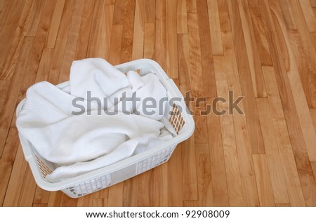 Clean white towels in a laundry basket, on a wooden floor indoors.