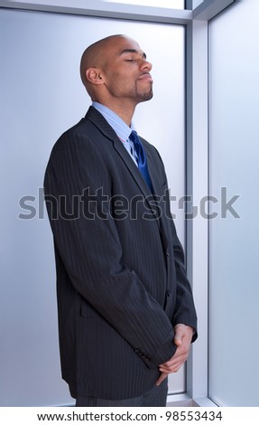 Businessman looking zen, standing with his eyes closed near a window.