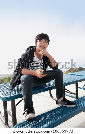 young boy sitting on picnic table with tablet pc smiling