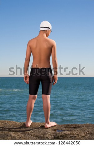 Young swimmer standing on stone and looking to sea water