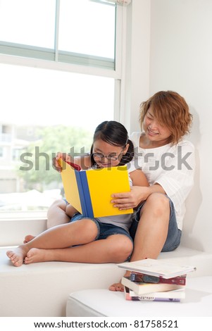 mom and daughter reading book on window sill