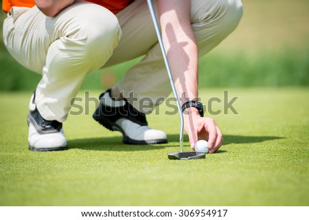 Man is concentrating to hit the golf ball on the putting green with his golf club. Trying to find out the best way to hit it.