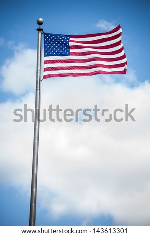 Vertical view of an American flag blowing in the wind against the clouds