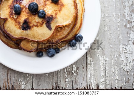 Stack of blueberry pancakes on a plate with blueberries on a rustic wooden table