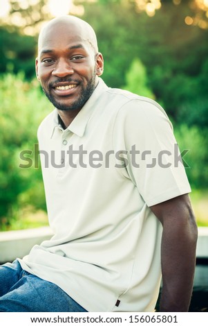 Portrait of a handsome late 20s black man sitting at the park on a summer day