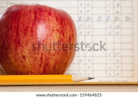Red apple on a book with pencil and vintage report card in background