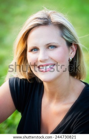 Headshot portrait of an early 30s casual happy beautiful blond woman at the park on a sunny summer day