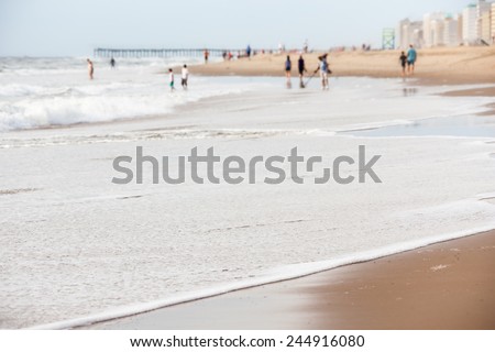 Tourists in the water at Virginia Beach with pier and hotels on beachfront property on a summer day