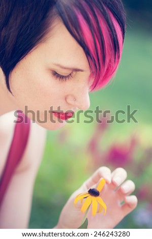 Beautiful punk woman with pink hair plucking flower petals for he loves me, he loves me not decision with faded desaturated filtered effect