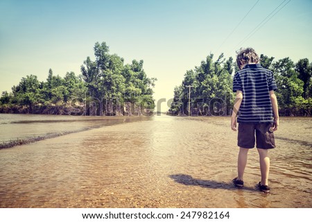 Child standing on flooded road in rural America after a springtime flood with vintage filtered effect