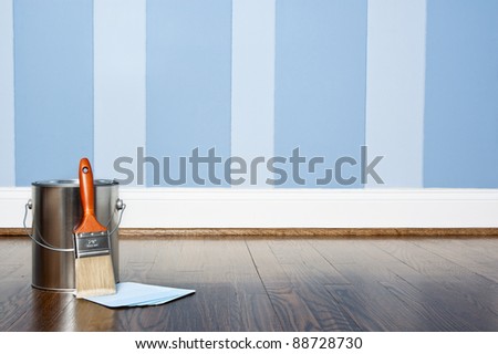 Paint can and brush against a blue striped wall