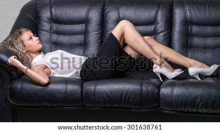 very beautiful, sensual sexy blonde girl lying on a balck sofa, close-up