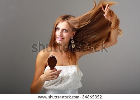Flying hair. Attractive young lady with comb on a gray background.