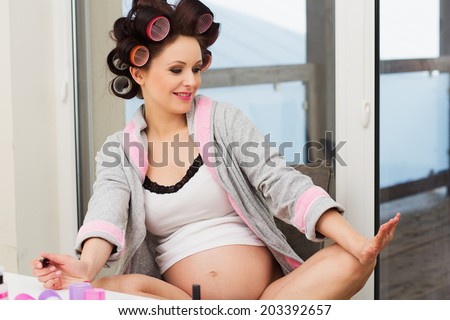 Pregnant woman with hair rollers getting nail treatment