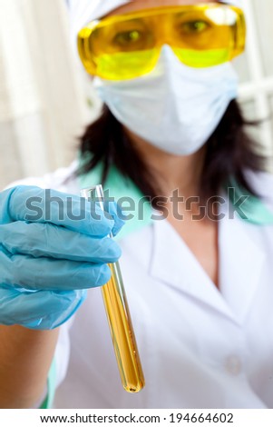 A female medical or scientific researcher or woman doctor shows a test tube of yellow solution in a laboratory
