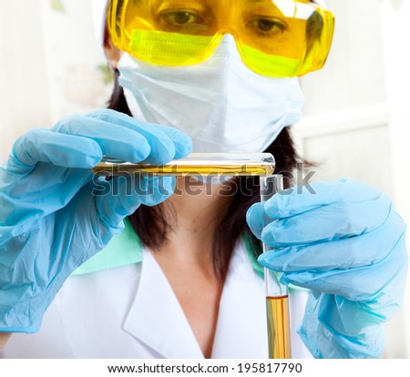 a female medical or scientific researcher or woman doctor looking at a test tube of yellow solution in a laboratory