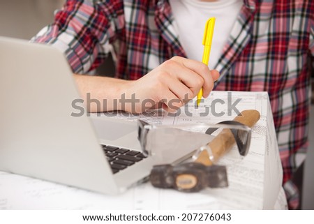 foreman hands with pen over documents and drawings, between the laptop and hammer
