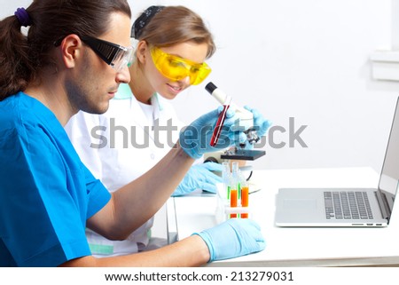 Two scientists in the lab are studying the contents of the test tubes and observe under the microscope