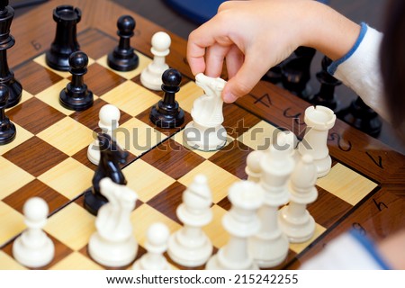 the child\'s hand with chess pieces on the board