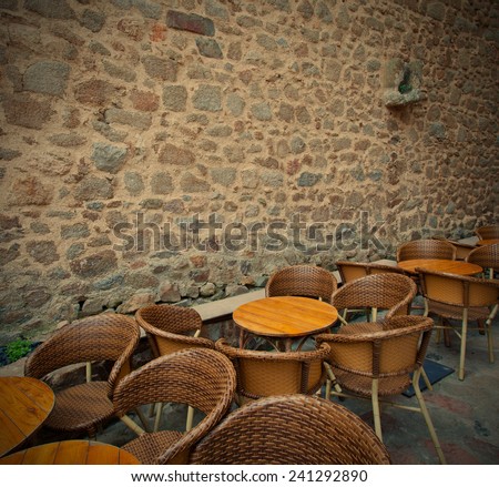 tables and wicker chairs in summer cafe near the ancient stone wall, instagram image style