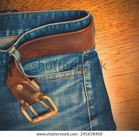 Aged blue jeans with a leather belt on wooden boards. copy space. instagram image style